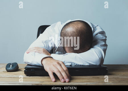 An exhausted young caucasian businessman is sleeping over his laptop in office. Stock Photo