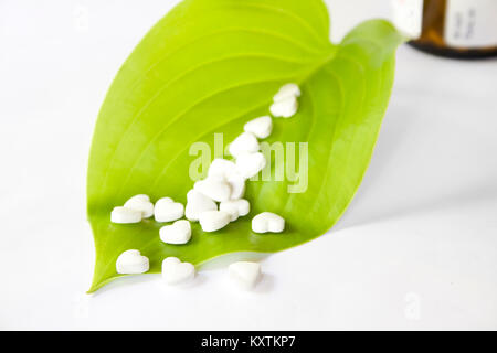 White medical cardiological pills in the form of heart on a green leaf. The drug for restoring health. A bottle of brown glass in the background Stock Photo