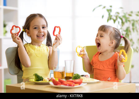 Funny playful children girls eating healthy food. Kids lunch at home or kindergarten. Stock Photo