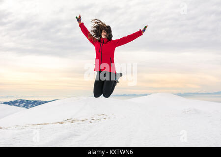 Happy girl hiker jumping on snow covered mountain top Stock Photo