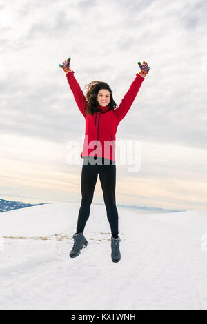 Happy girl hiker jumping on snow covered mountain top Stock Photo