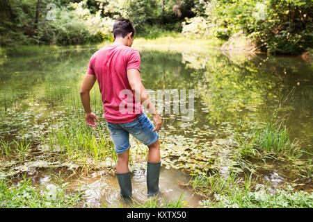 Teenage boy in rubber boots standing in lake. Stock Photo