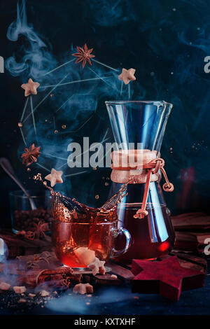 Glass coffee cup with a dynamic splash and rising steam with a donut constellation. Hourglass-shaped coffeemaker on a dark background with copy space. Stock Photo