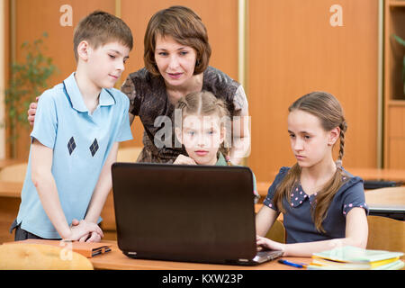 Kids group and their teacher looking at laptop screen in classroom Stock Photo