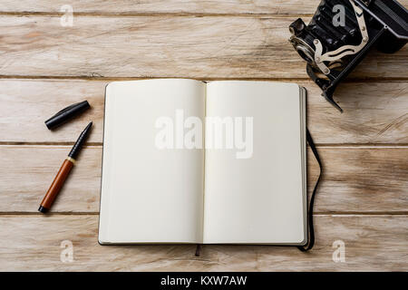 high-angle view of an open notebook with a blank space, a pen and an old folding film camera on a white rustic wooden table Stock Photo
