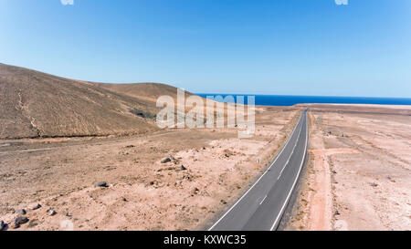 Aerial view of long road through volcanic desert landscape towards Atlantic Ocean, Fuerteventura, Canary Islands, Spain . Stock Photo