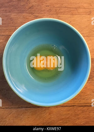 Double yolk chicken egg in blue bowl on wooden cutting board Stock Photo