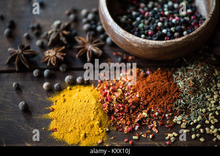 different kinds of pepper in bowl and spices with herbs scattered on wooden tabletop Stock Photo