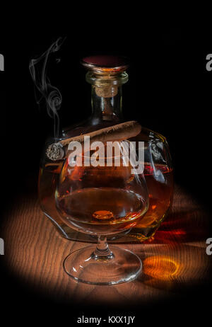 A glass of cognac with a cigarette lit against a bottle Stock Photo