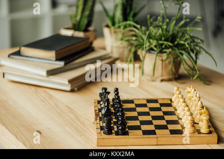 Chess board set for a new game on the table with books and potted plants  Stock Photo