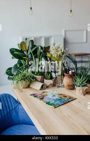 Wooden table full of potted green plants and art supplies  Stock Photo