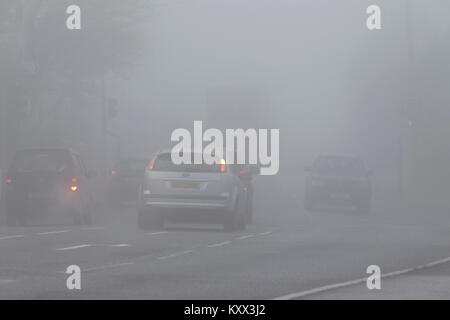 cars at a road junction some with no lights on foggy day in the uk Stock Photo