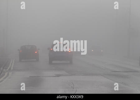 cars driving along city street with foglights on foggy day in the uk Stock Photo
