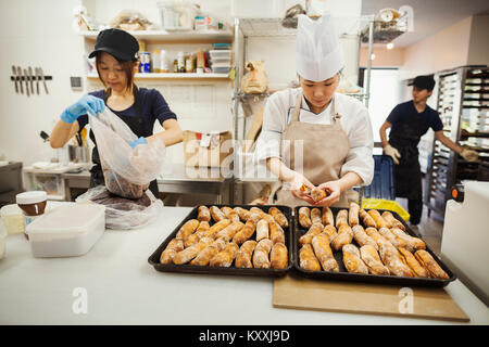 Two women and man working in a bakery, preparing freshly baked rolls on large trays. Stock Photo