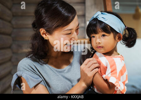 Smiling woman holding young girl with black pigtails wearing blue hairband. Stock Photo