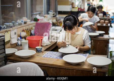 Women sitting in a workshop, working on Japanese porcelain bowls. Stock Photo