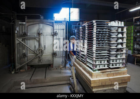 Interior view of Japanese porcelain workshop, man preparing large stack of porcelain objects for kiln. Stock Photo