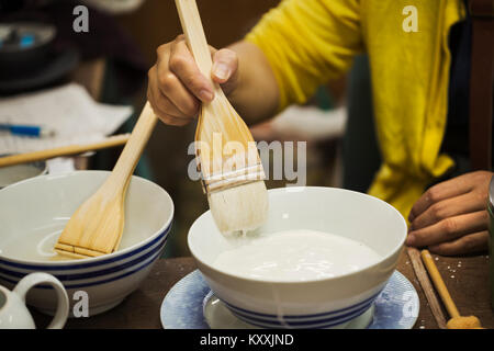 Close up of person working in a Japanese porcelain workshop, glazing white bowls with paintbrush. Stock Photo