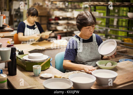 Two women sitting in a workshop, working on Japanese porcelain bowls. Stock Photo