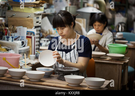 Two women sitting in a workshop, working on Japanese porcelain bowls. Stock Photo