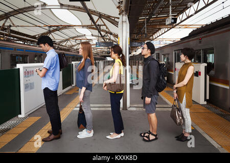 Five people standing in a row on a subway platform, waiting in line, Tokyo commuters. Stock Photo