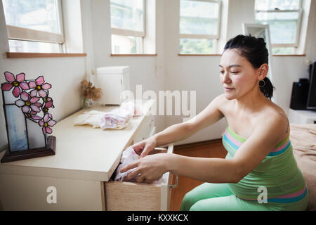 A pregnant woman in a baby's nursery room, folding baby clothes. Stock Photo