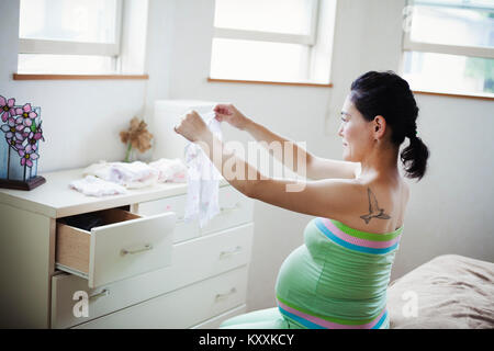 A pregnant woman in a baby's nursery room, folding baby clothes. Stock Photo