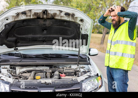 Worried young man examining his car engine parked on the side of a road Stock Photo