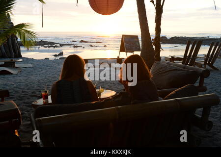 The setting sun makes a perfect back drop for drinks at a beachside bar Stock Photo