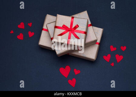 Gift boxes decorated with red ribbons with bows lie on a black background, as well as red hearts lined around boxes Stock Photo
