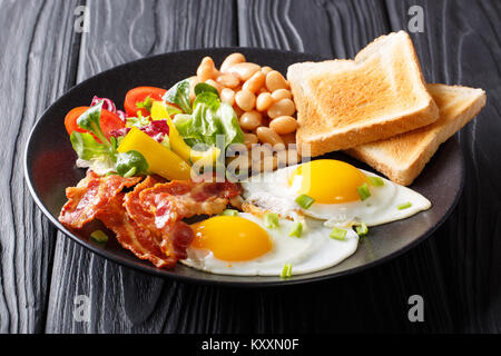 Delicious and hearty meal: two fried eggs with bacon, beans, toast and vegetable salad on the table. Classic breakfast. horizontal Stock Photo