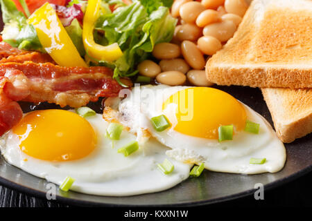 English breakfast macro: fried eggs, bacon, beans, toast and fresh vegetable salad on a plate. horizontal Stock Photo
