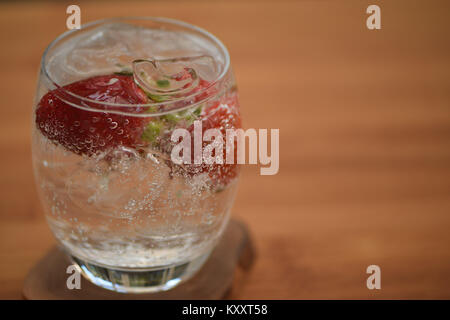 food and drink close up photography image of a glass of ice cube sparkling bubbly water with fresh fruit whole strawberry on wood background space Stock Photo