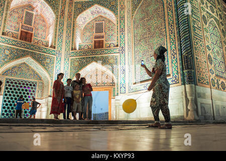 Women take pictures in front of the madrasah Tillya-Kori in the registan square in Samarkand Stock Photo