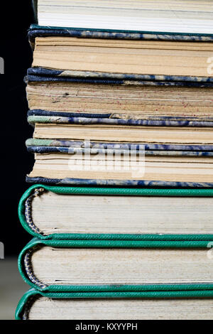 The spines of old books lying on the stack. Books stacked on an old table. Black background. Stock Photo