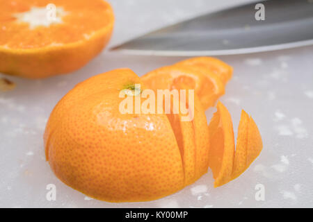Tangerine being sliced on a cutting board with seeds and knife Stock Photo