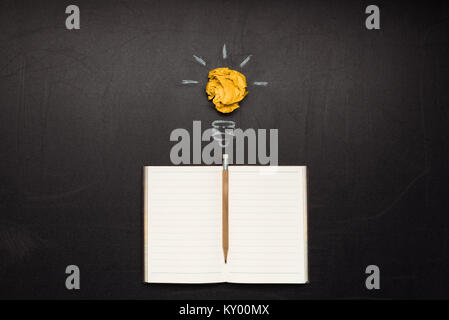light bulb symbol and blank notebook with pencil on blackboard Stock Photo