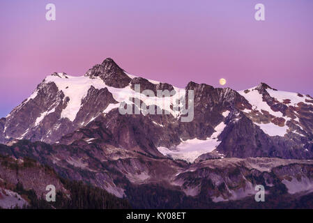 A full moon rises over Mt Shuksan in October as the setting sun turns the sky pink and purple Stock Photo