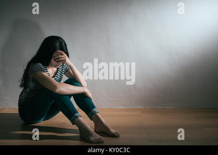 beautiful pretty woman having depression bipolar disorder emotion problem sitting on wooden floor in white wall background. Stock Photo