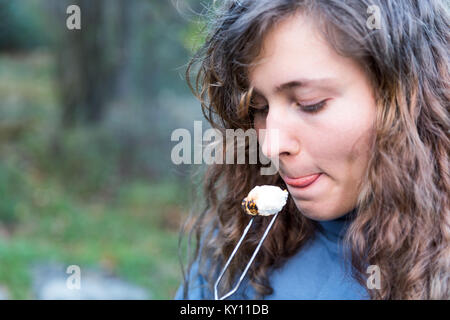 Young woman eating roasted caramelized marshmallow skewer closeup macro portrait licking lips, tongue Stock Photo