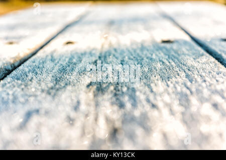 White frost ice crystals on wooden picnic table in morning sunlight macro closeup with shiny sparkling bokeh Stock Photo