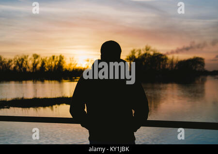 Silhouette of man overlooking flooded fields in the Whittlesey fens at sunset. Stock Photo