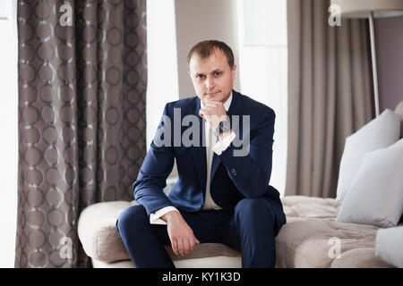 Man the groom in suit sitting on sofa in hotel Stock Photo