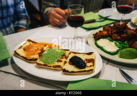 Traditional tapas plate with grilled cheese with canarian sauces mojo rojo, mojo verde and alioli, and glasses of red wine on background, Tenerife, Ca Stock Photo