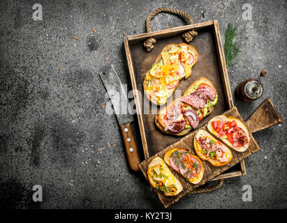 Various sandwiches with seafood, meat and vegetables on an old tray. On a rustic background. Stock Photo