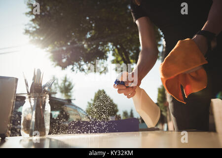 Worker spraying water while cleaning table Stock Photo