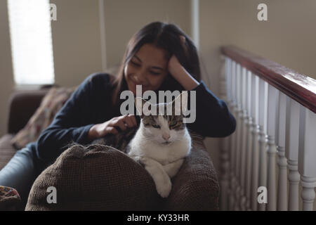 Teenage girl sitting with cat on sofa in living room Stock Photo