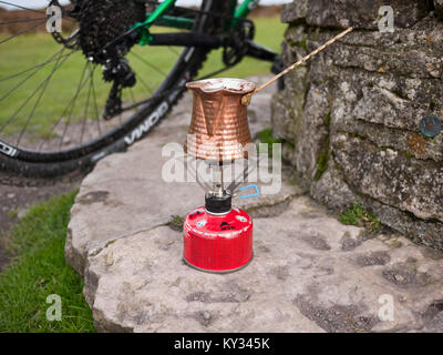 Making turkish coffee with a traditional copper ibrik on a gas camping stove on the Long Mynd in the Shropshire Hills, UK Stock Photo