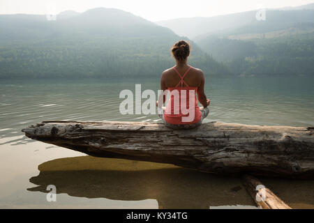 Fit woman sitting in meditating posture on a fallen tree trunk