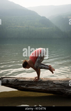 Fit woman performing a hand stand on a fallen tree trunk Stock Photo